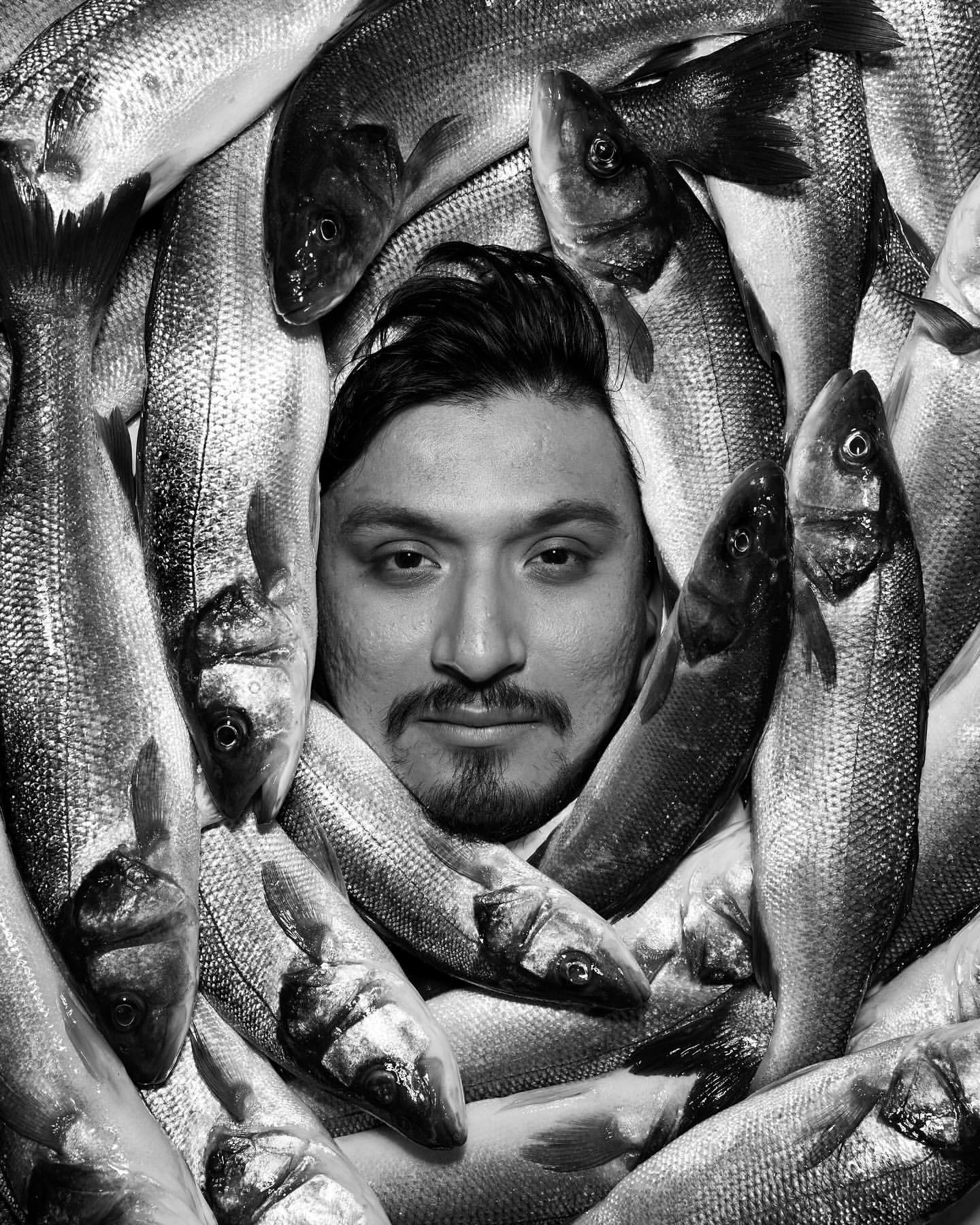 Portrait of a man surrounded by fresh fish in a black and white composition, creating a striking and unusual visual effect.