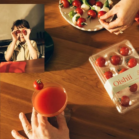 Overhead shot on a wood table with tomatoes, mozzarella, basil skewers, a cocktail, packaged tomatoes, and a girl playfully holding tomatoes.