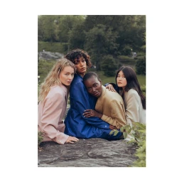 Four women in pastel and blue blazers posing closely together on a rocky outdoor ledge surrounded by trees.