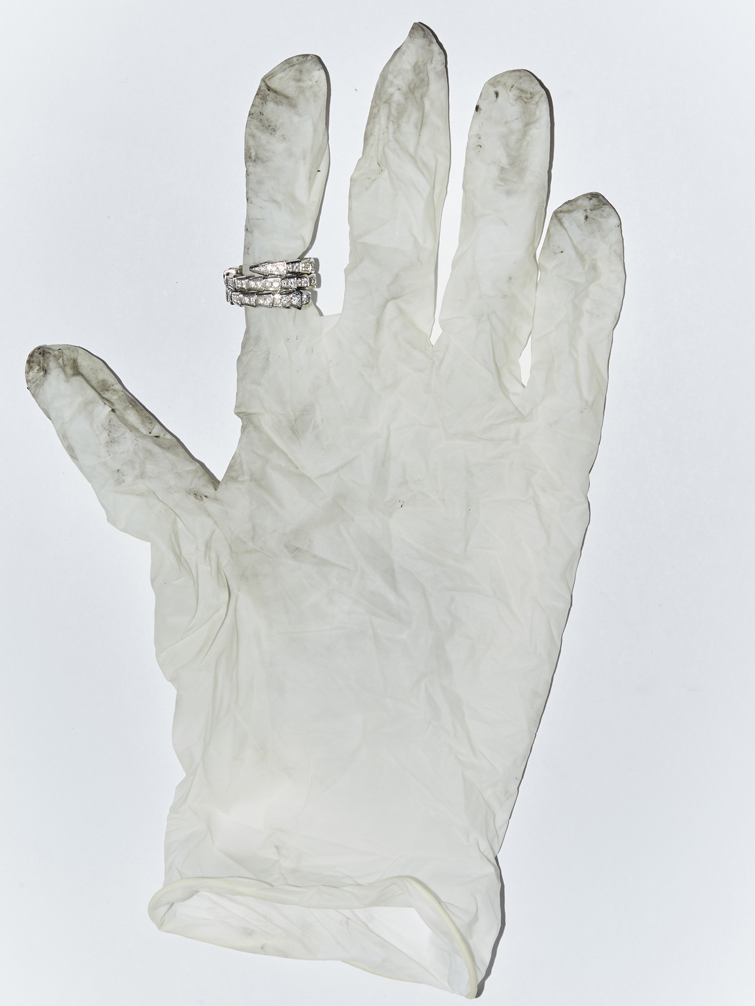 Three diamond rings displayed on the index finger of a dirty, white, latex glove against a plain, white backdrop in a studio shot.