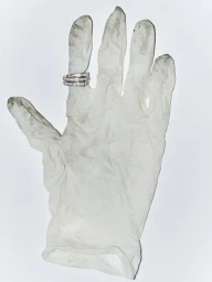 Close-up of a used white rubber glove with smudges and dark stains, wearing three diamond rings on the index finger.