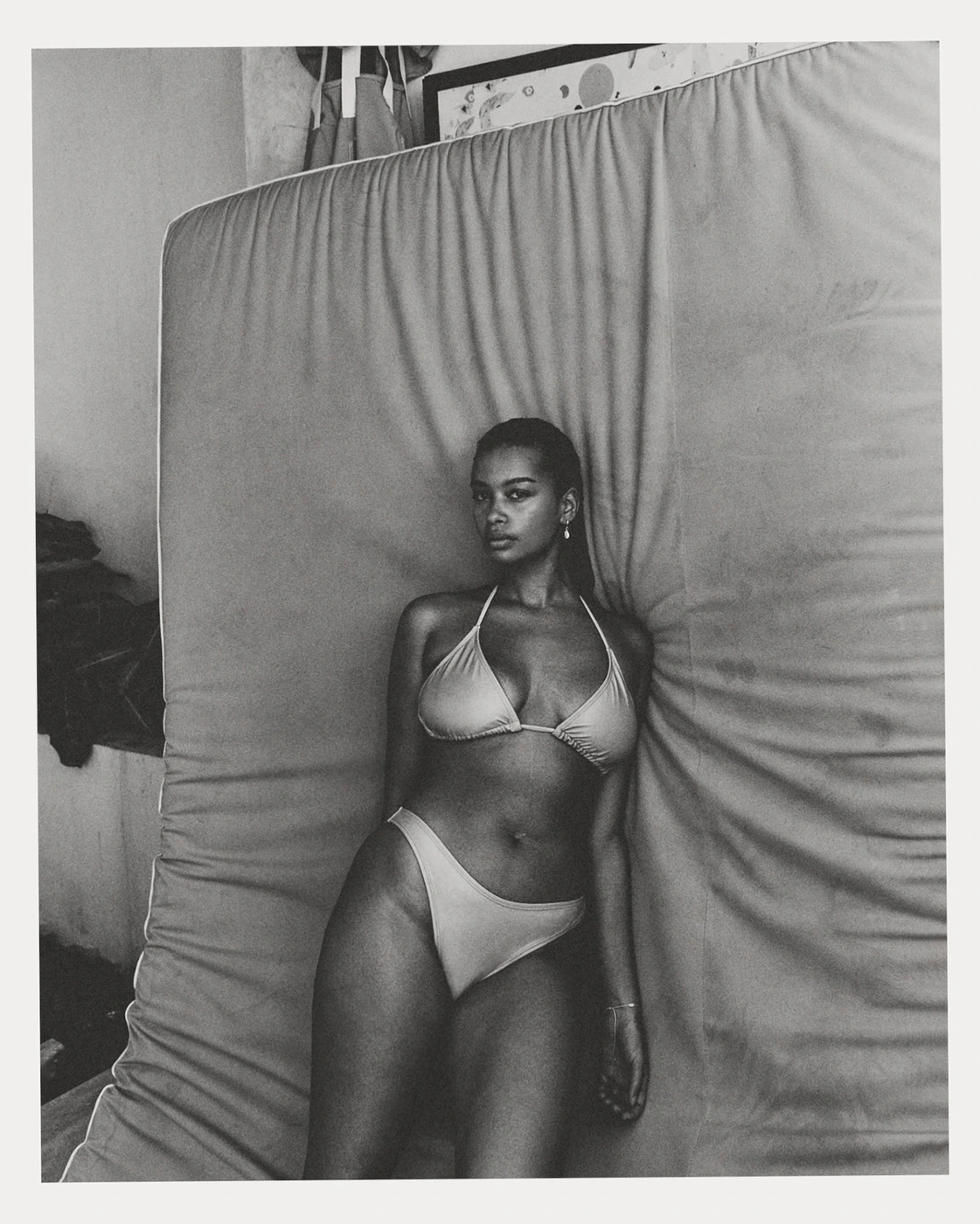 Black and white portrait of a woman wearing a bikini, leaning against a large textured mattress in Sydney by Pierre Toussaint.