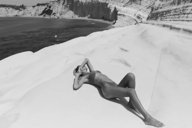 Model lying on white rock formations by the ocean in a bikini photographed by Pierre Toussaint