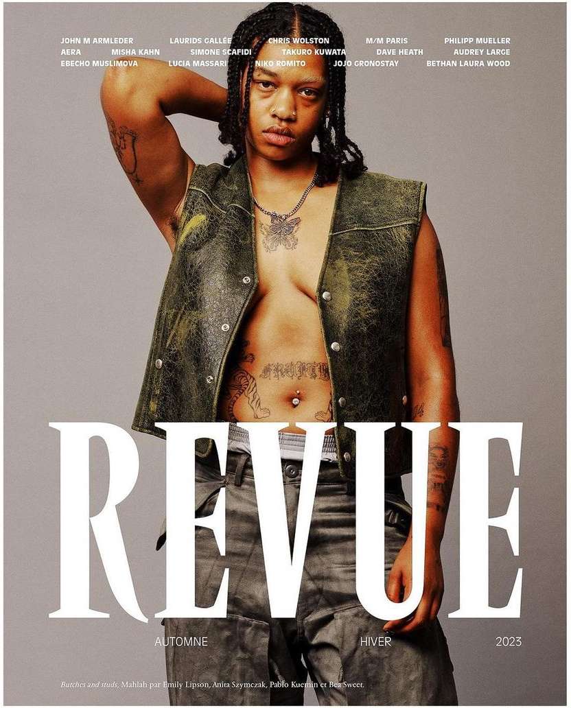 Revue magazine cover featuring a shirtless non-binary model with visible tattoos, leather vest, and gray jeans against a gray background.