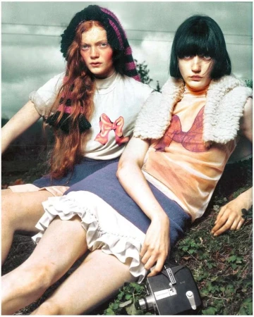 Two models sitting on grassy ground holding a vintage film camera by Emily Lipson