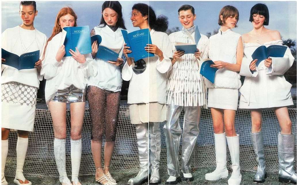 Seven models in white and silver outfits holding Mozart books. The fashion shot features a group standing in a line for editorial purposes.