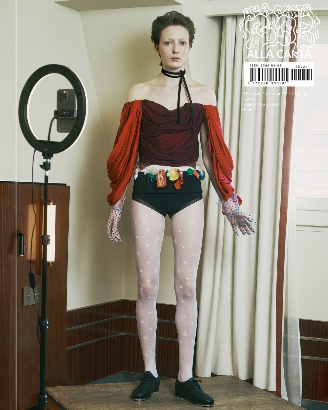 Young woman in a haute couture fashion shoot wearing black shoes, sheer white patterned stockings, black high-waisted briefs, and a maroon top.