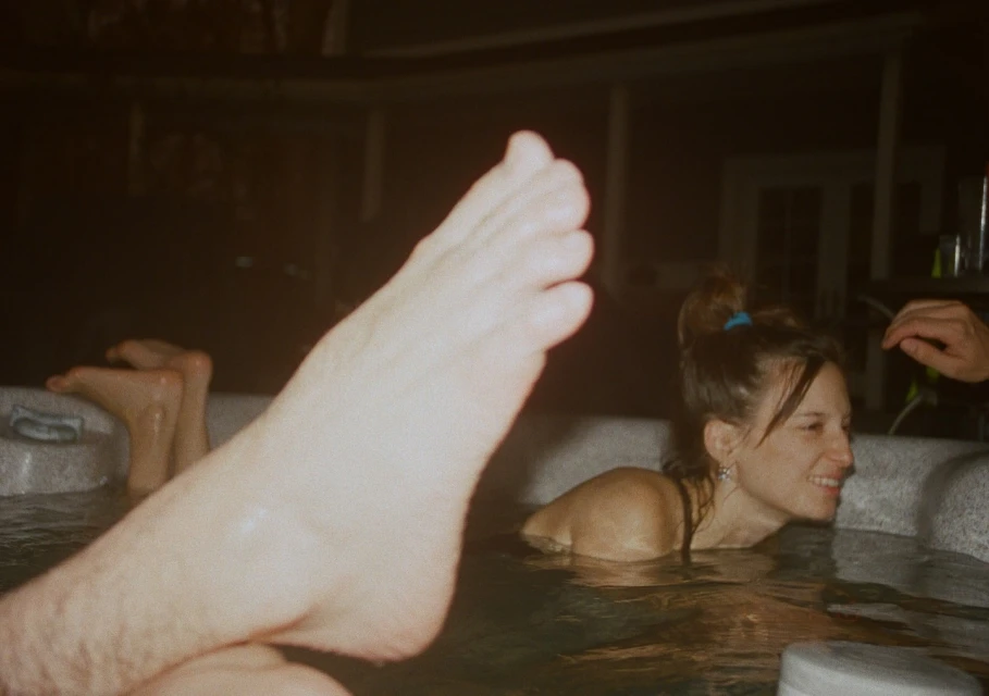 Smiling woman relaxes in a warm hot tub with water reflecting lights, creating a cozy and inviting atmosphere in a dark setting.