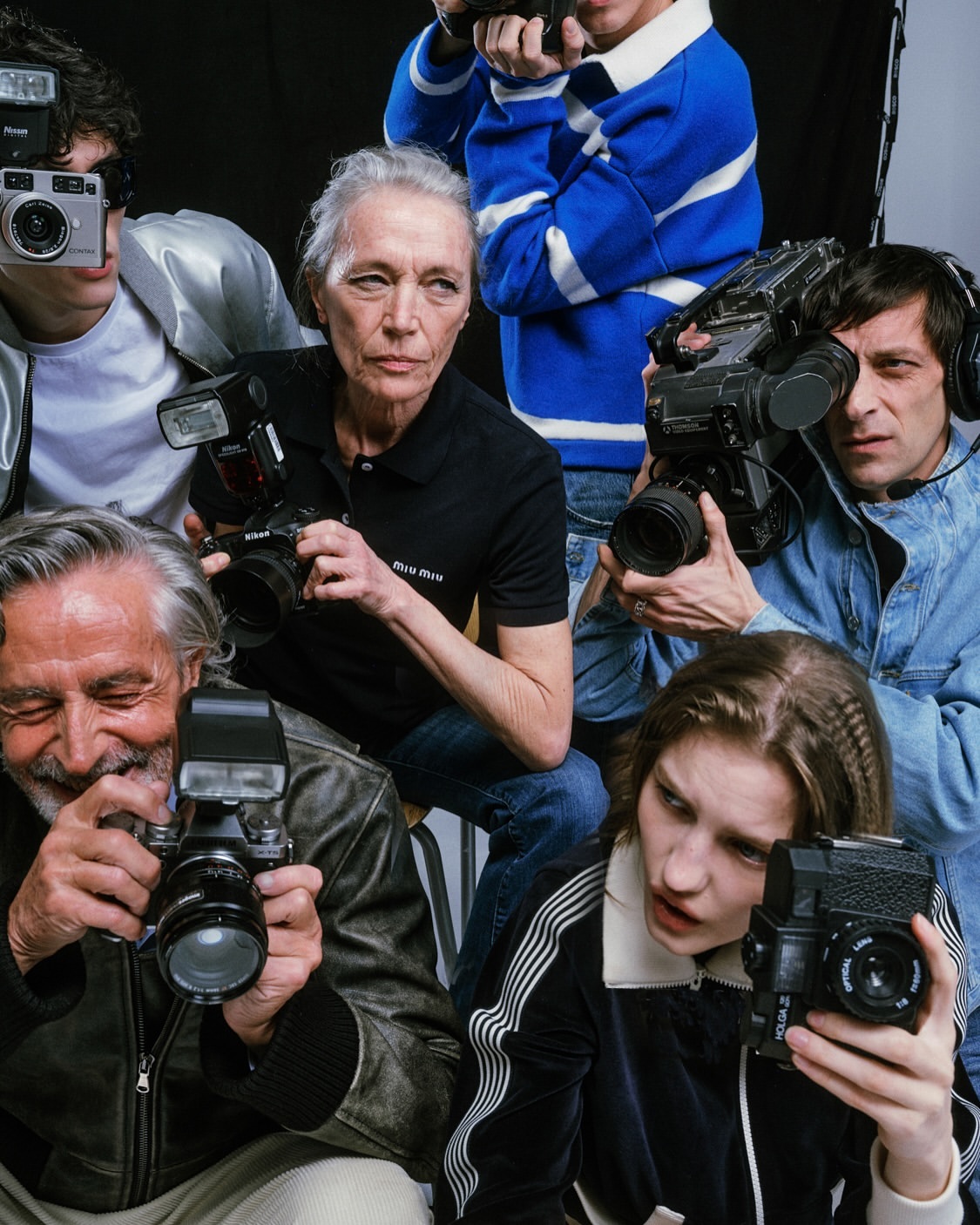 Group of people, including older and younger adults, holding various film cameras, video cameras, and cameras with flash attachments in studio.
