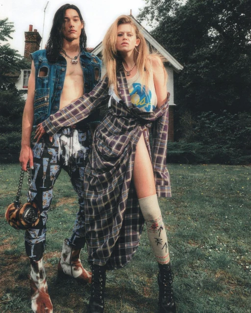 A fashion editorial presents a man and woman in alternative 90s-inspired outfits in a grassy, outdoor setting with a house behind them.