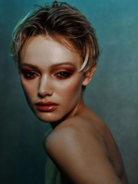 Portrait of a fair-skinned adult female with short hair and reddish eye shadow looking at the camera against a muted green backdrop.