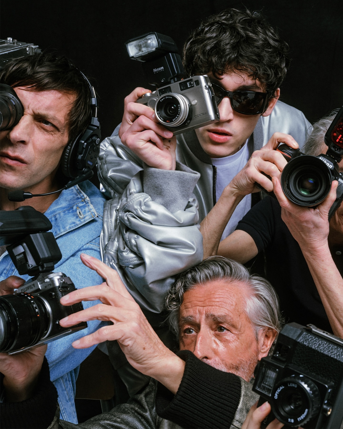 Multiple photographers taking pictures with vintage and modern cameras in a crowded setting, showcasing diverse ages and equipment.