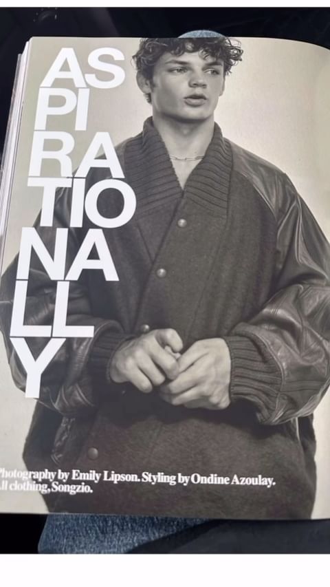 Fashion editorial photograph of a young adult male model wearing an oversized jacket, posing on the magazine page, looking away. 