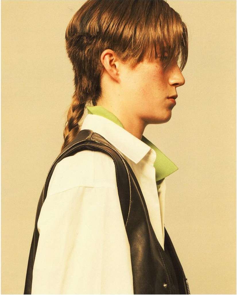 Profile shot of a person with medium brown hair styled in a braid and wearing a white collared shirt and a black vest.