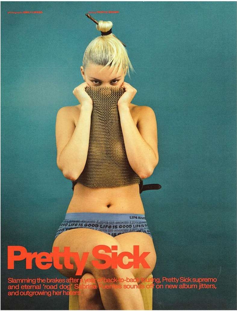A young blonde woman with unique hairstyle poses in a fashion editorial, wearing blue underwear and covering her chest with metal mesh.
