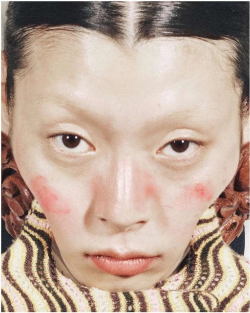 Extreme close-up of an Asian woman with pink blush, a striped turtleneck, and large wooden earrings, creating a vibrant, beauty-focused image.
