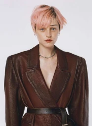 Portrait of a person with pink hair wearing a dark brown leather blazer against a white background