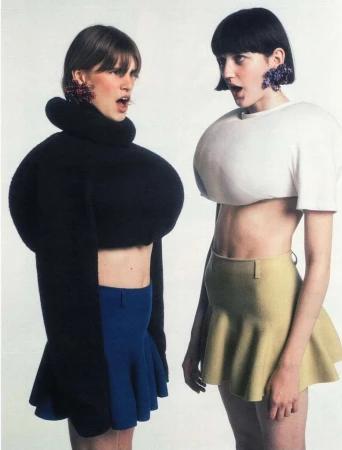 Two models with exaggerated sculptural tops and dark bobs posing against a plain background by Emily Lipson.
