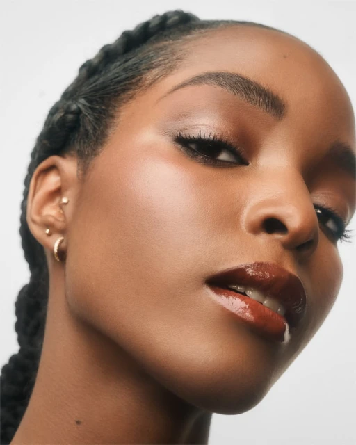 Close-up studio shot of a woman with braided hair, wearing glossy lip color, against a plain white background.