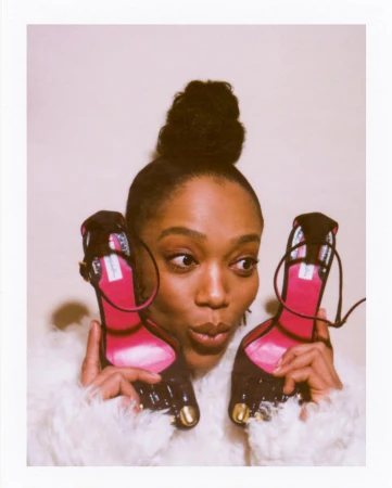 Woman holding up two high heel shoes framing her face against a plain background