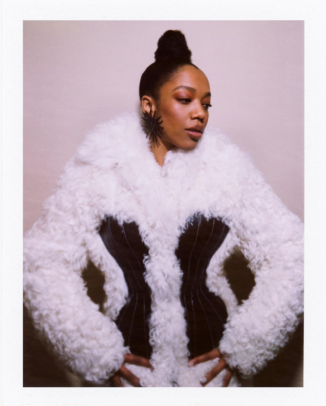 Elegant portrait of a woman with an updo hairstyle, wearing a dramatic black and white fur coat and sculptural earrings in a studio setting.