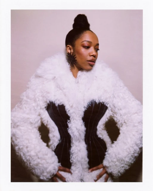 Elegant portrait of a woman with an updo hairstyle, wearing a dramatic black and white fur coat and sculptural earrings in a studio setting.