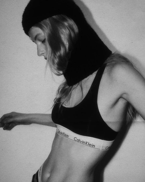 Monochrome portrait of a fair-skinned adult female wearing a black sports bra and dark balaclava, angled towards the camera.