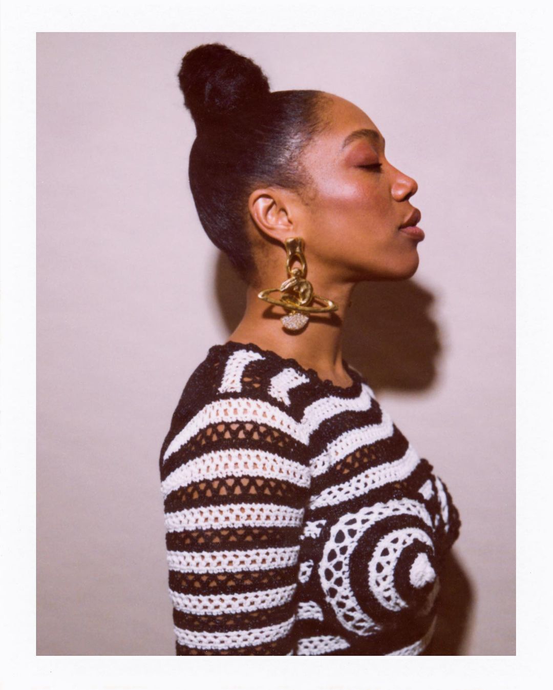 Profile view of an adult female with her hair in a high bun, wearing a black and white striped crochet sweater and large gold earrings.