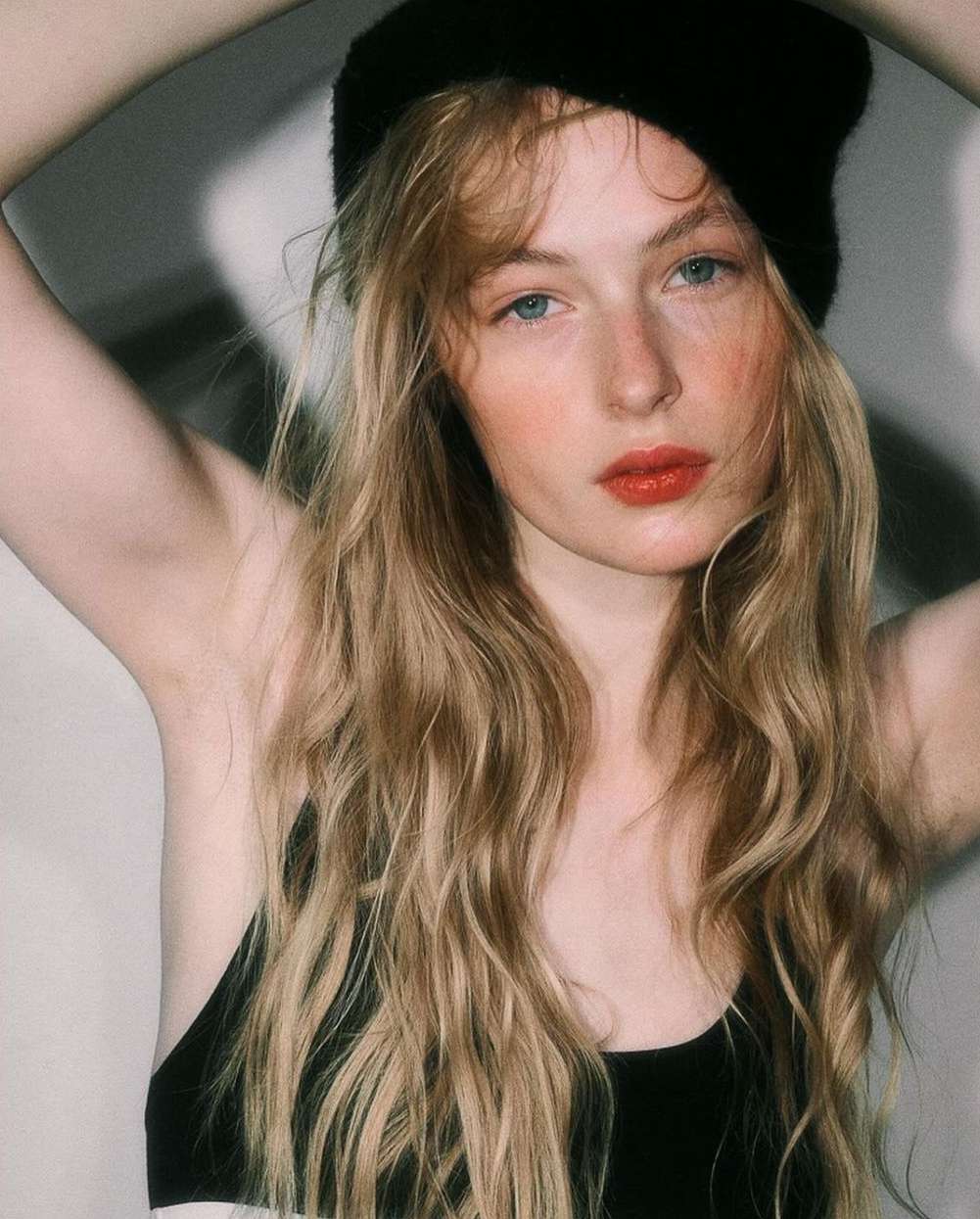 Portrait of a young woman with fair skin, light blonde hair, wearing a black beanie and top, posing indoors with neutral expression.