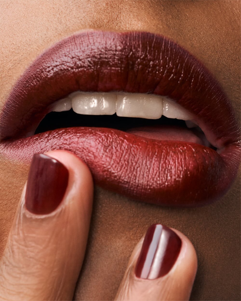 Close-up of a person with dark skin and red lipstick touching their lower lip with their finger, showcasing glossy nails.