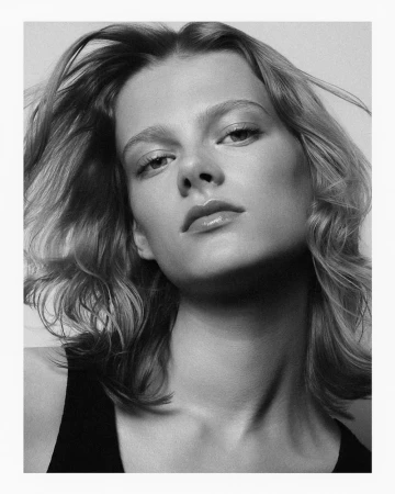 Monochrome portrait of a woman with tousled shoulder-length hair and a dark tank top against a plain light background