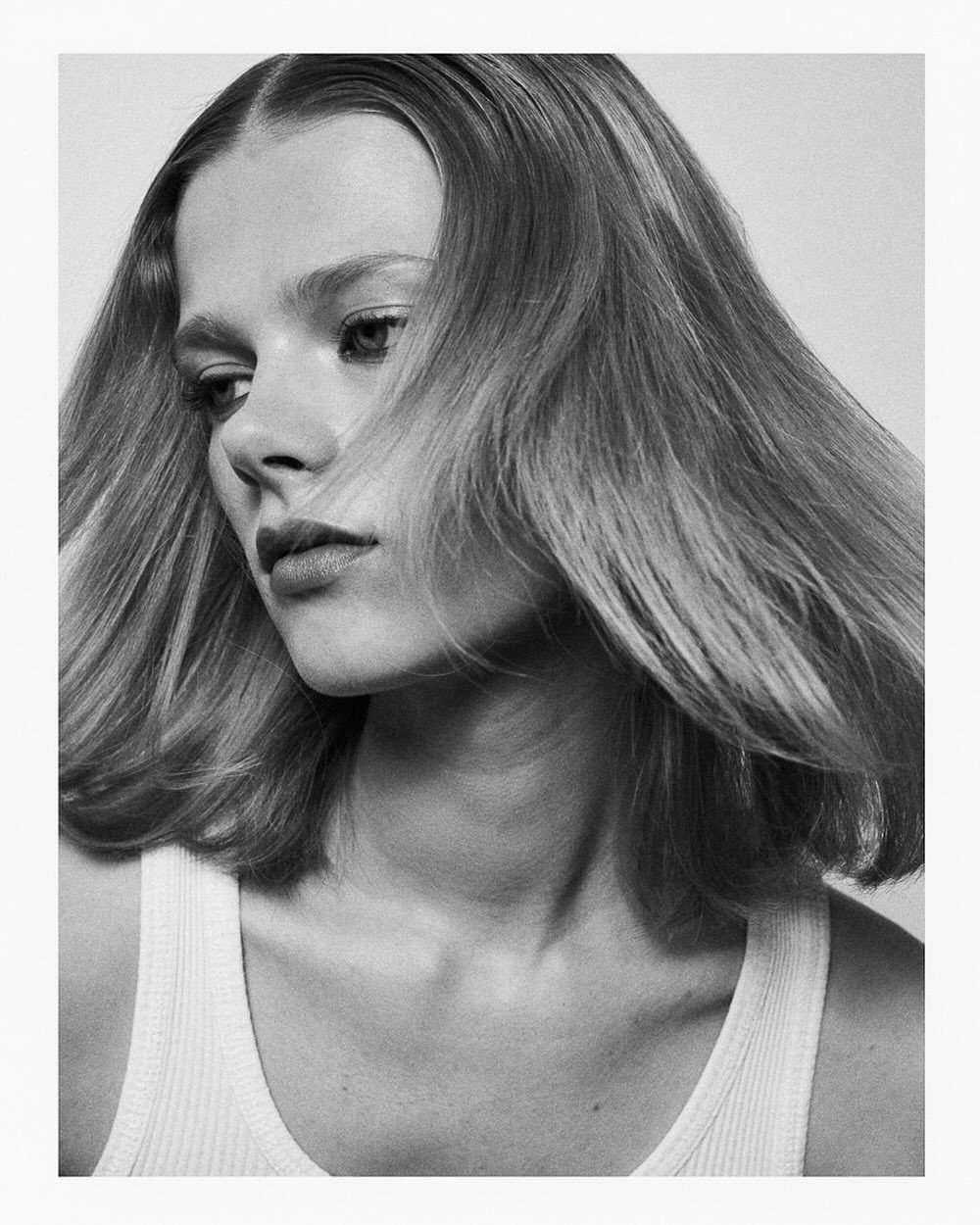 Black and white portrait of a woman with medium length hair wearing a white ribbed tank top against a plain light background