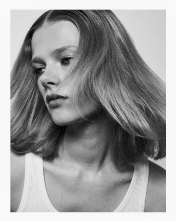 Black and white portrait of a woman with medium length hair wearing a white ribbed tank top against a plain light background
