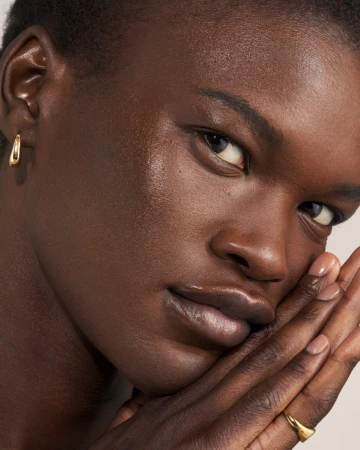 Close-up portrait of a Black woman holding her hands against her face wearing gold jewelry