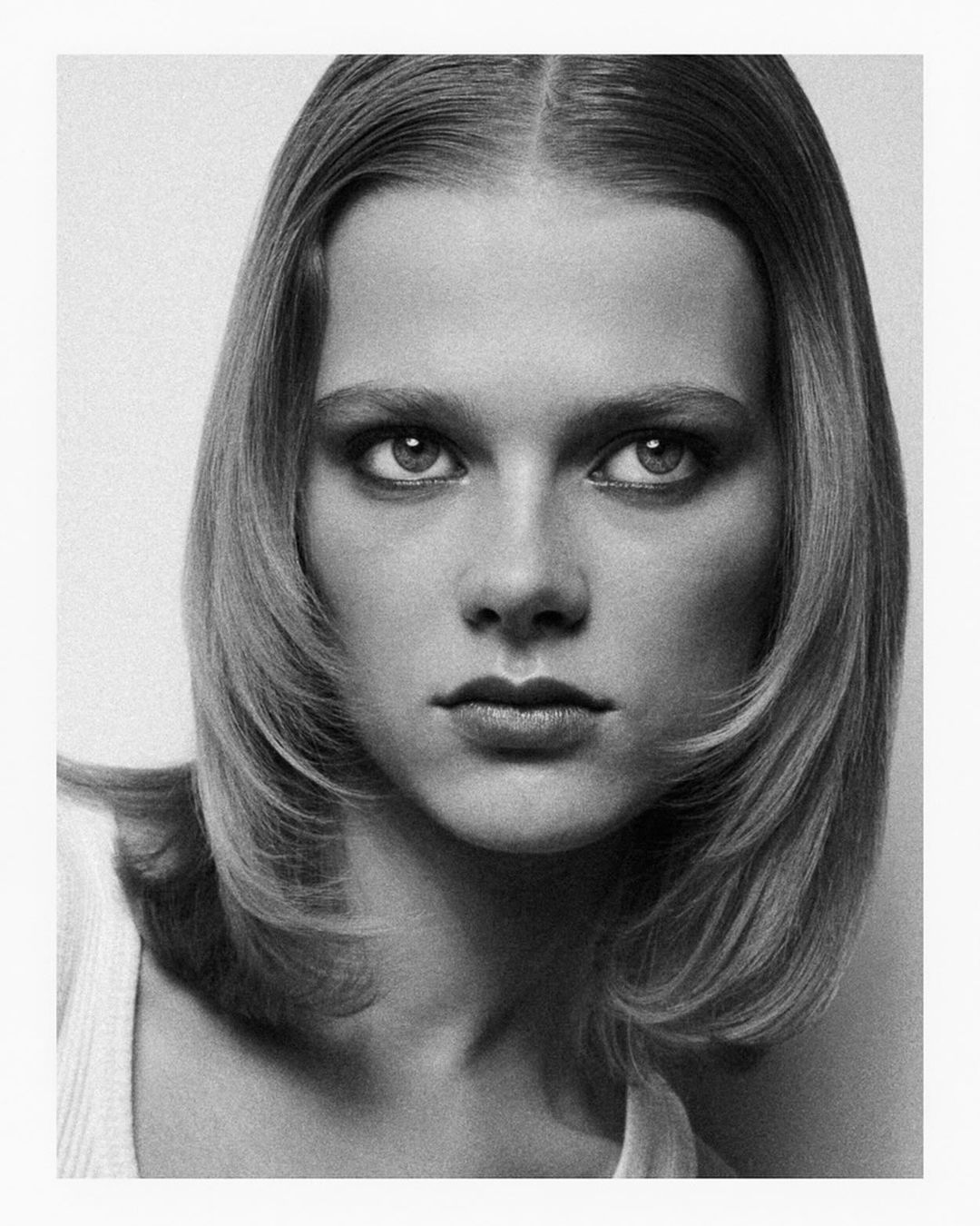 Close-up portrait of a woman with center-parted shoulder-length hair wearing a white top