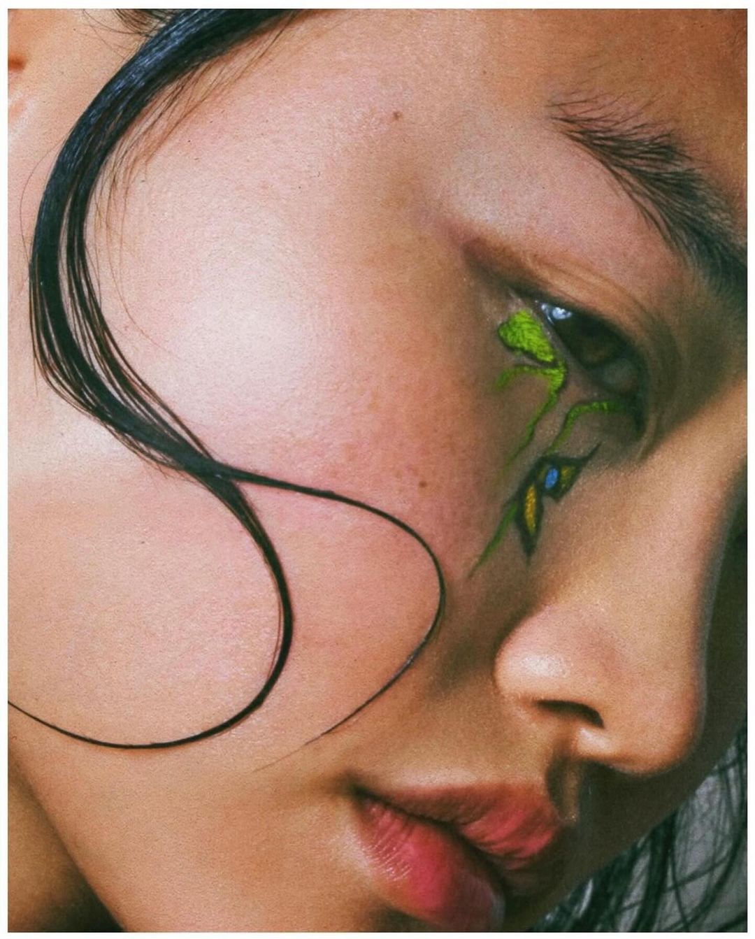 Close-up portrait of a woman with vibrant green eye makeup and wet dark hair strands across her face by Emily Soto.