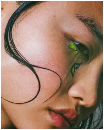 Close-up portrait of a woman with vibrant green eye makeup and wet dark hair strands across her face by Emily Soto.