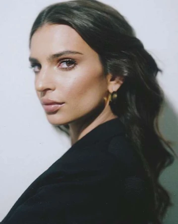 Portrait of a woman with dark wavy hair wearing a black blazer against a light wall in New York