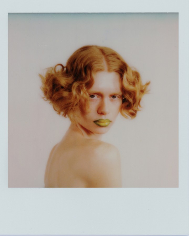 Portrait of a young adult female with red, wavy hair and yellow lipstick, posing in a studio setting with soft, diffused lighting.