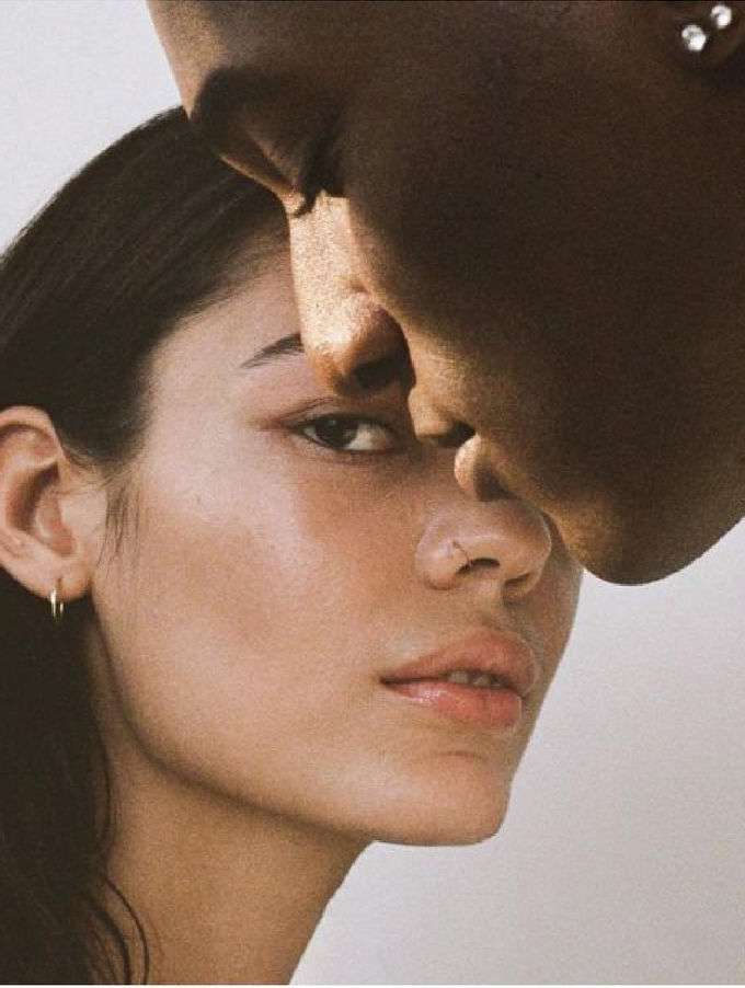 Close-up portrait of two faces: a woman with light skin and a man with dark skin, showcasing skin tones and facial features against a light background.