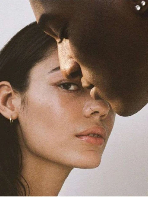 Close-up portrait of two faces: a woman with light skin and a man with dark skin, showcasing skin tones and facial features against a light background.