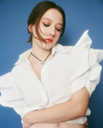 Close-up portrait of a woman wearing a white collared shirt with ruffled sleeves against a blue background, by Emily Soto.