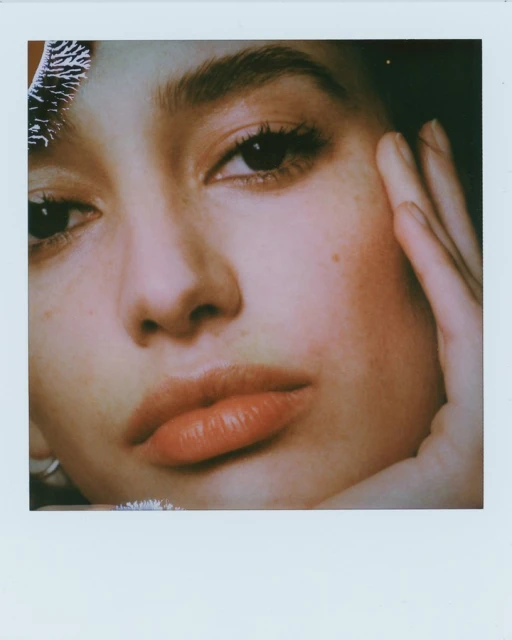 Close-up portrait of a young adult woman's face with dark eyes and full lips, touching her cheek with her fingers in a photo studio.