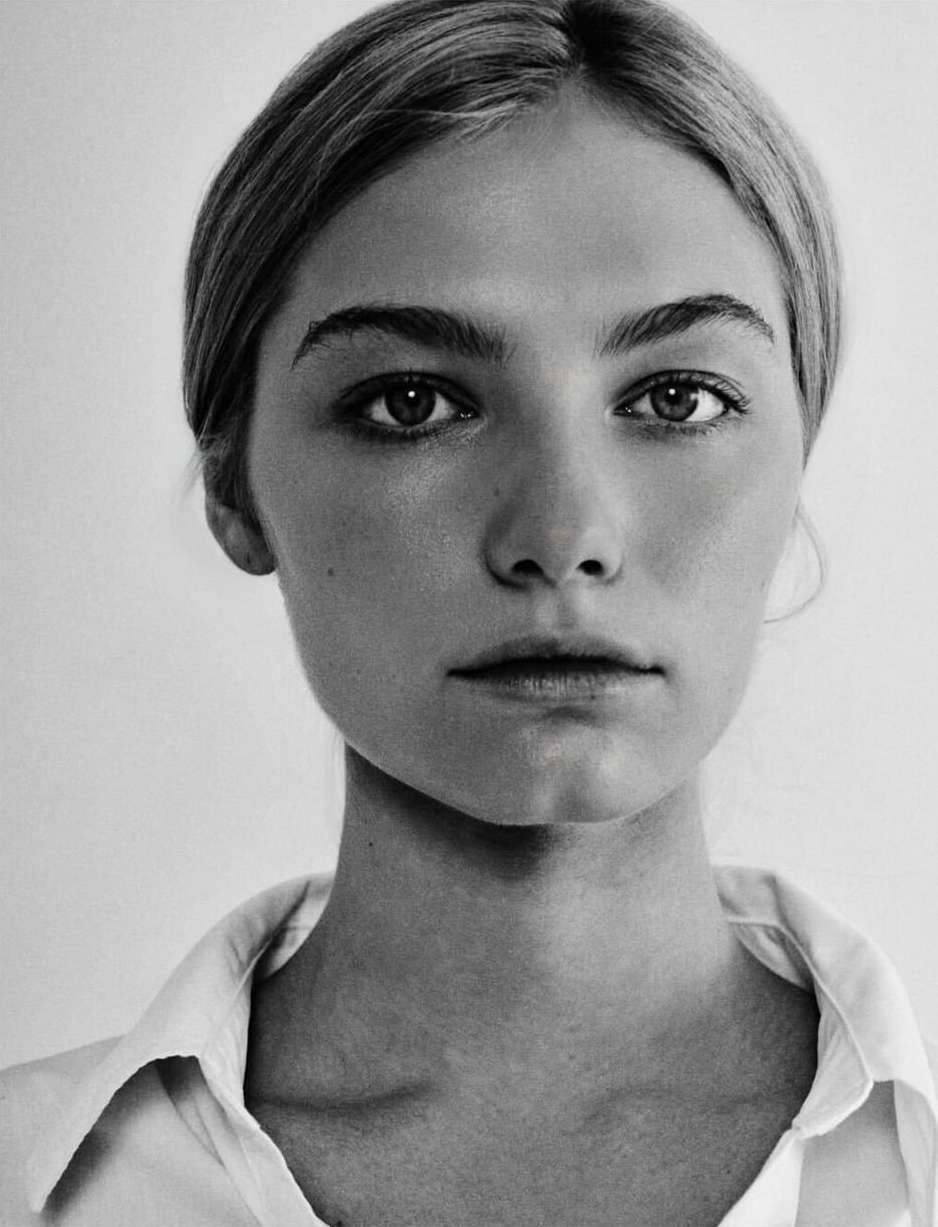 Monochrome portrait of a young fair-skinned woman with blonde hair pulled back, wearing a collared shirt against a white background.