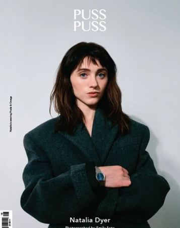 Portrait of Natalia Dyer wearing Prada and Omega on a magazine cover, medium shot on light grey studio background.