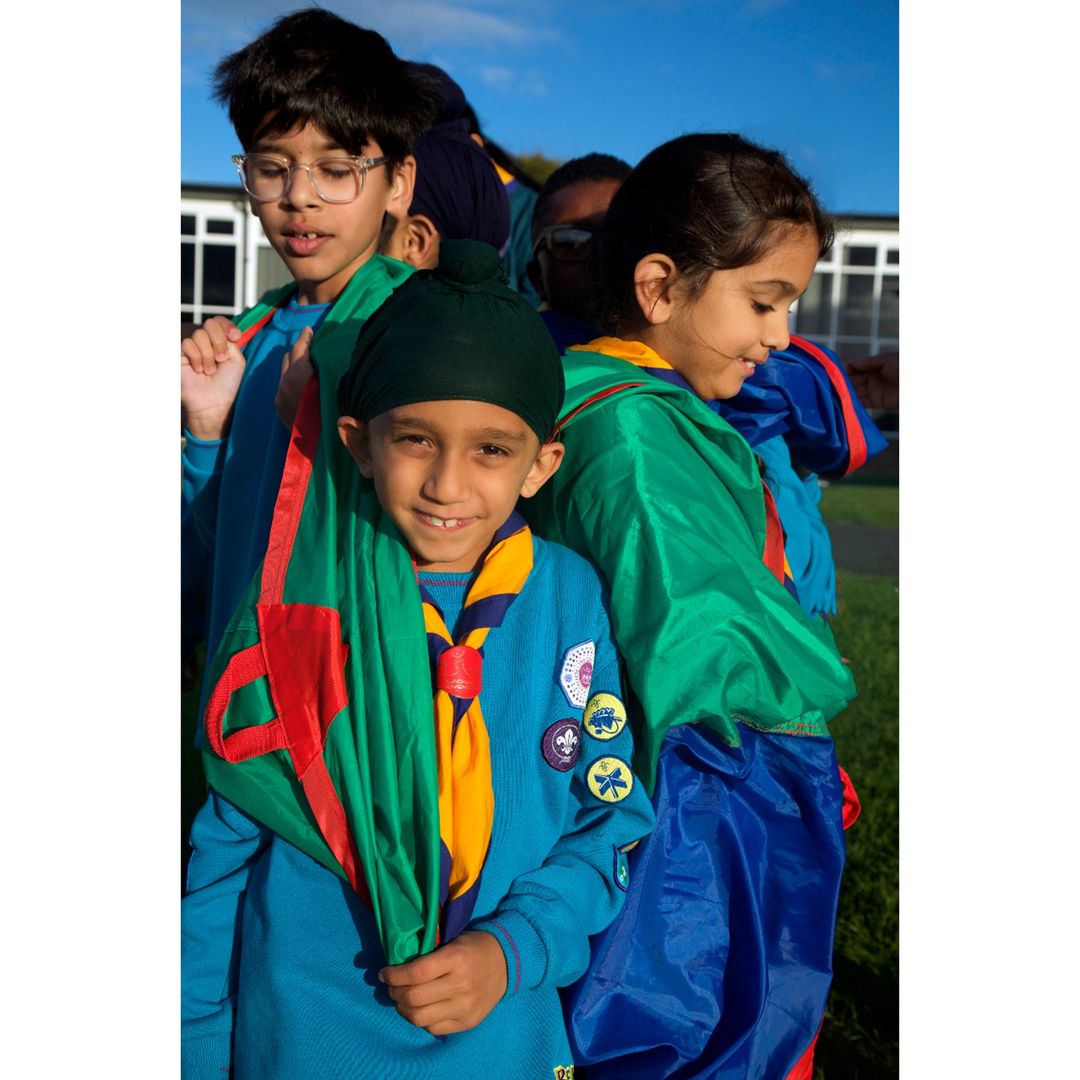 Group of children wearing uniforms and neckerchiefs outdoors under a blue sky, some smiling at the camera.