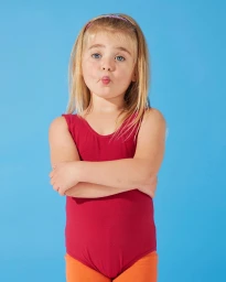 Young child in a red leotard crossing arms with a playful expression against a vibrant blue studio backdrop