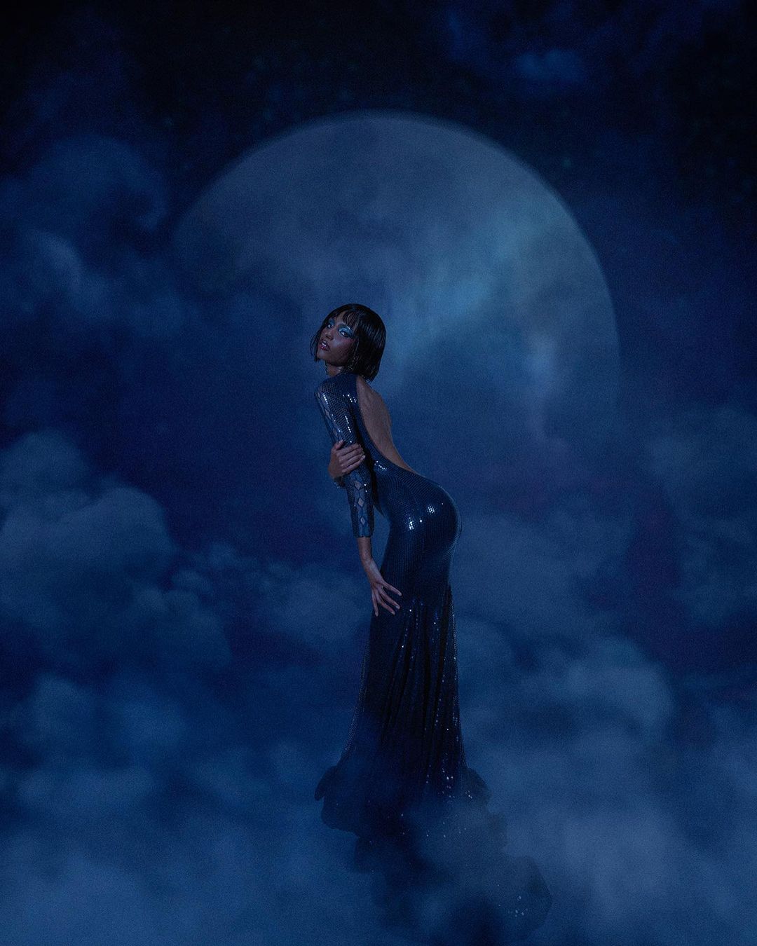 Woman in a long, blue, sparkly dress posing against a blue, cloudy backdrop with a large, bright moon in the background.