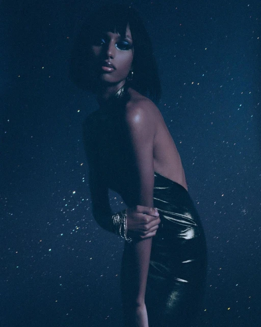 Glamorous portrait of an African American woman in a shiny dress. She poses against a dark blue background with star-like specks of light.