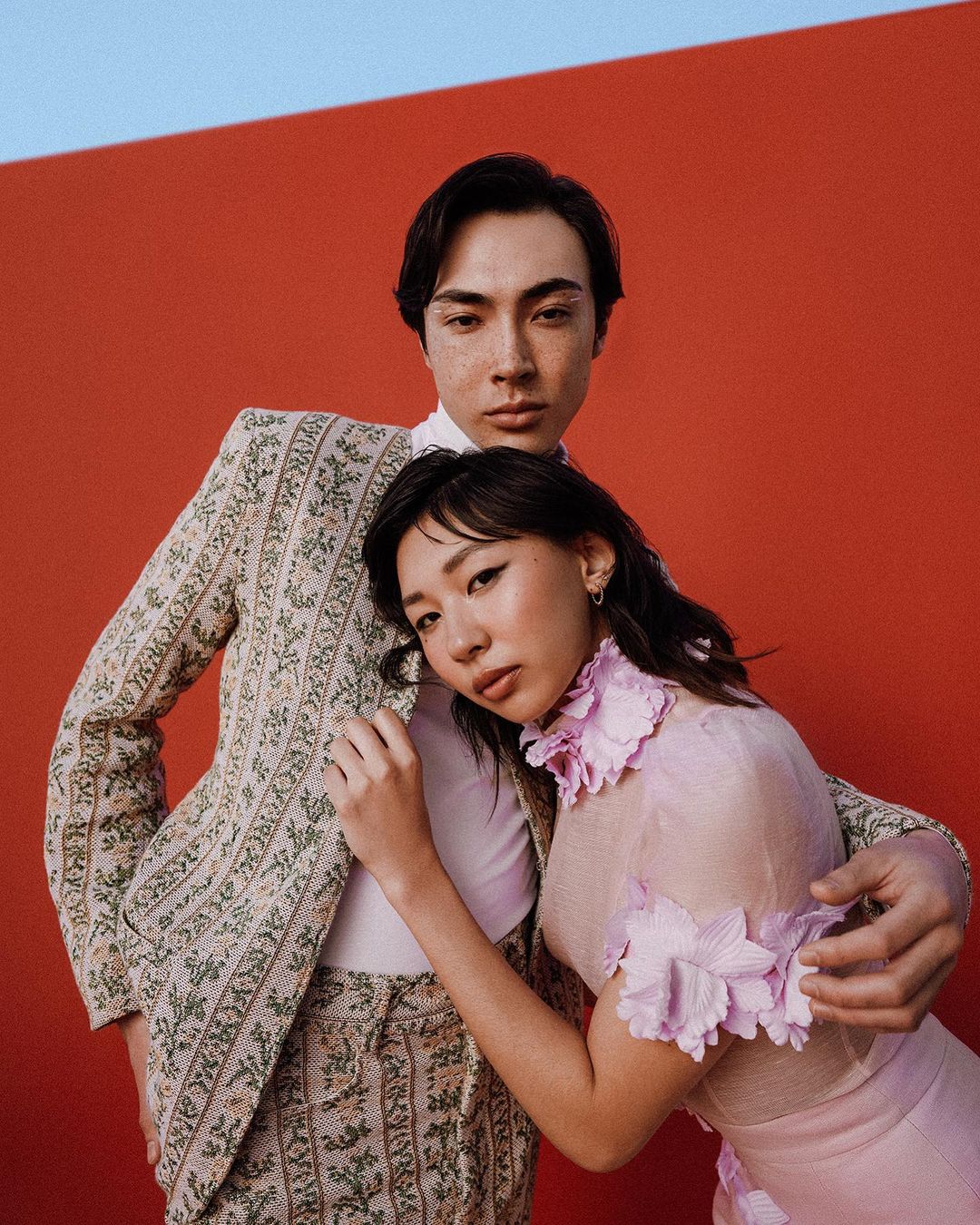 Portrait of an Asian couple in matching floral patterned suits against a bright red background in a studio setting with soft lighting.